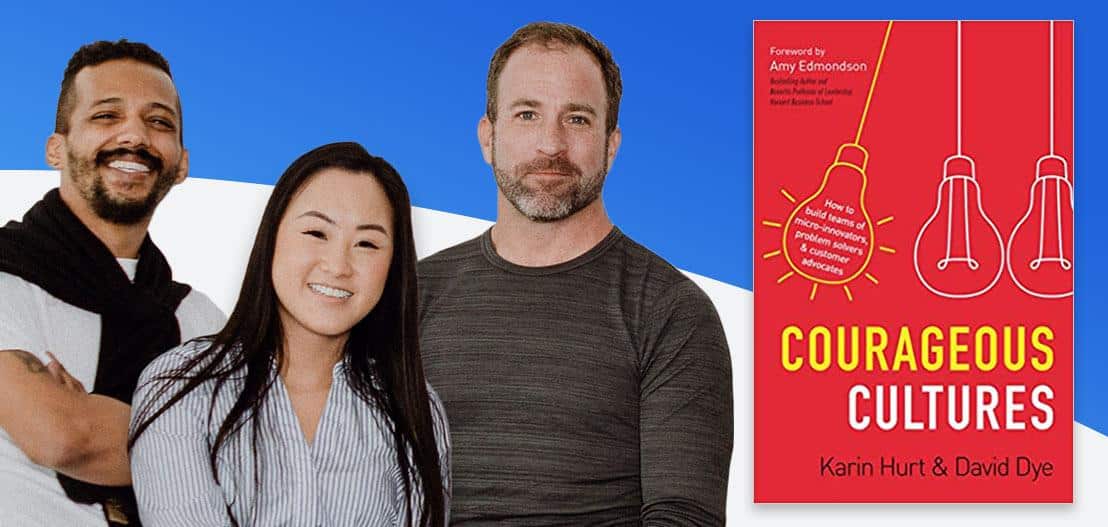 Three people stand smiling to the left of a book cover titled "Courageous Cultures," which vividly showcases illustrations of a light bulb and a pen on its striking red background.