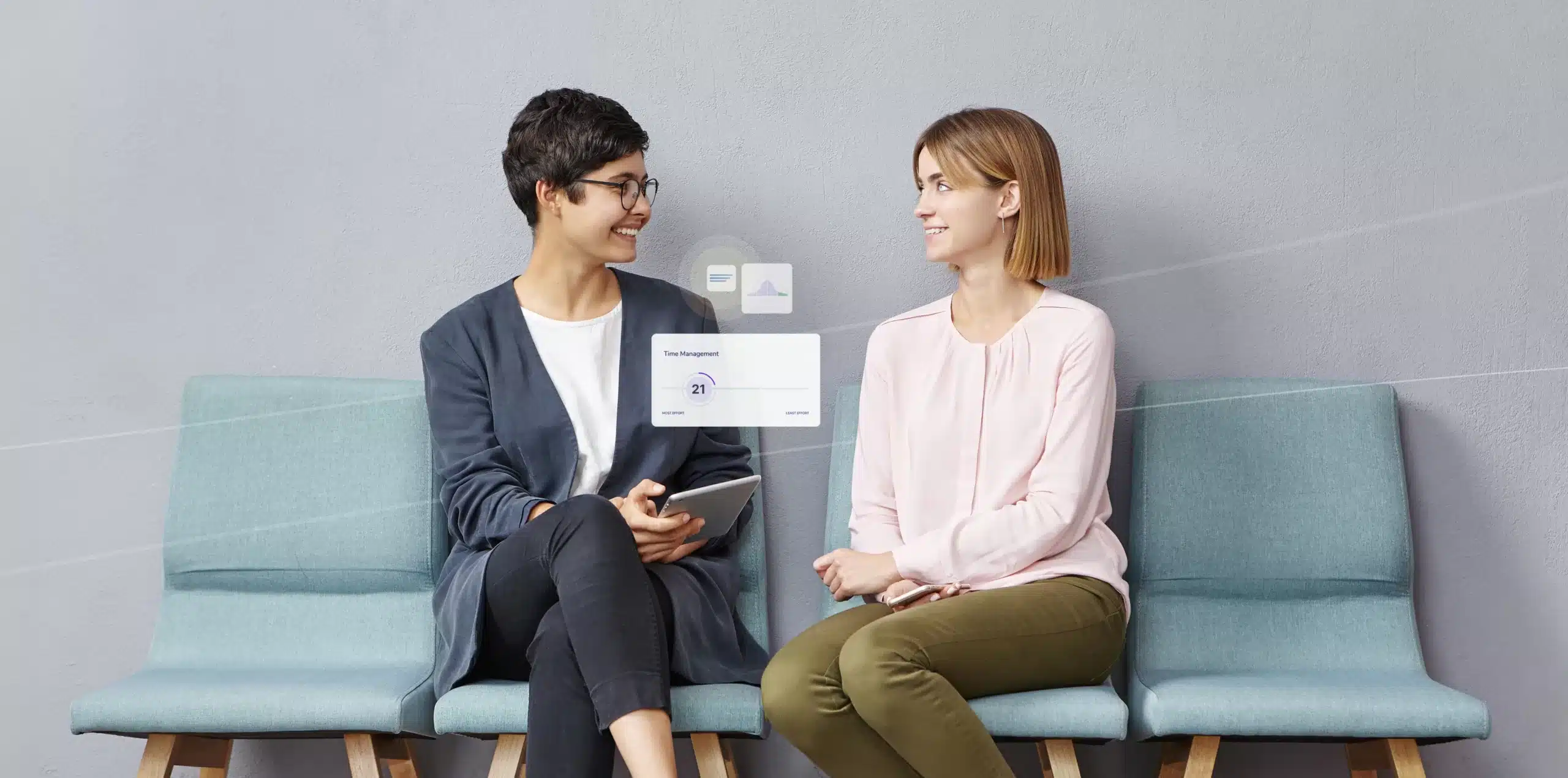 Two women sit on blue chairs against a gray wall, smiling and talking. One holds a tablet as digital graphics representing files and sharing appear, an inspiring moment of team development for leaders in action.