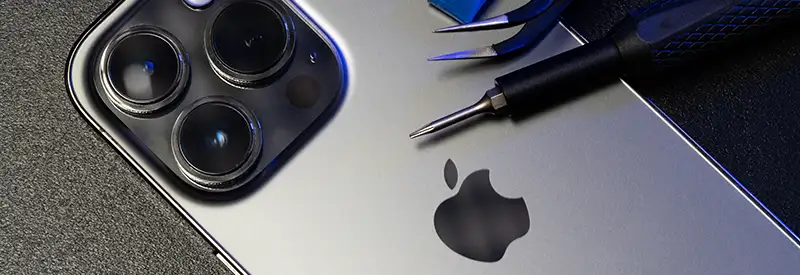 iphone-banner A close-up of the back of a silver iPhone with three camera lenses, placed next to precision screwdrivers and tools on a dark surface, highlights the Apple logo-symbolizing innovation fostered through strong team dynamics.