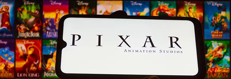 pixar-banner A smartphone displays the Pixar Animation Studios logo, held in front of a screen showing various colorful Disney animated movie posters, highlighting the team dynamics behind these beloved films.