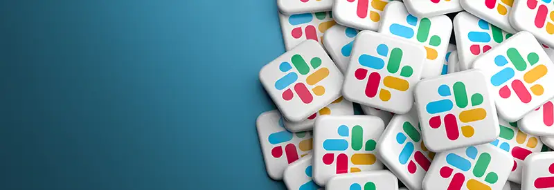 slack-banner A pile of square buttons displaying the colorful Slack logo, featuring overlapping bars in blue, green, yellow, and red, symbolizes vibrant team dynamics on a gradient blue background with empty space on the left.