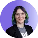 tonya-headshot Person with short, wavy hair dyed blue and green, wearing glasses, a gray shirt with a white design, and a black blazer, smiling in front of a purple gradient background-a look that reflects confidence and effective coaching expertise.