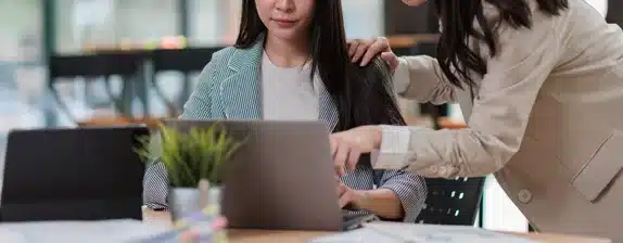 A woman points at a laptop screen to discuss employee career development while another woman looks on.