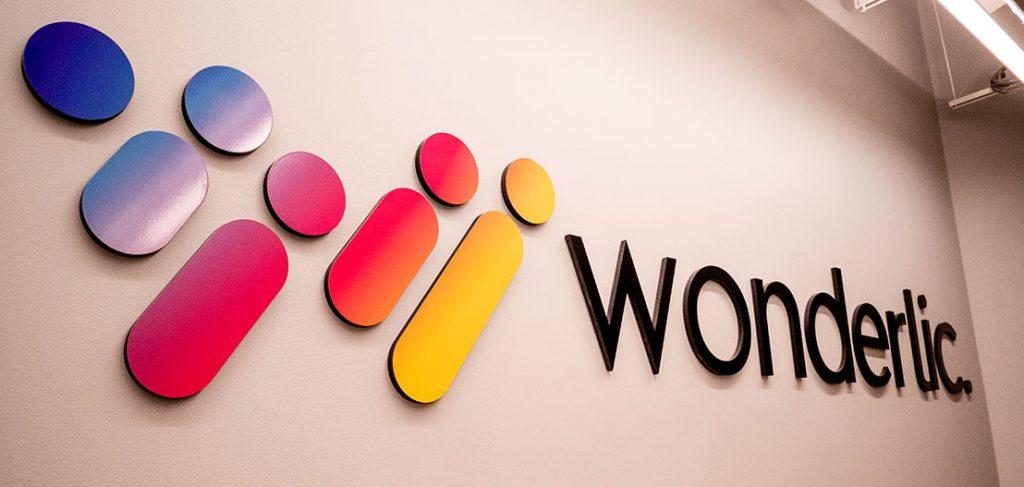 The image shows a wall with the word "Wonderlic" in black letters. To the left, there are abstract shapes resembling people, in gradient colors of blue, purple, pink, and yellow.