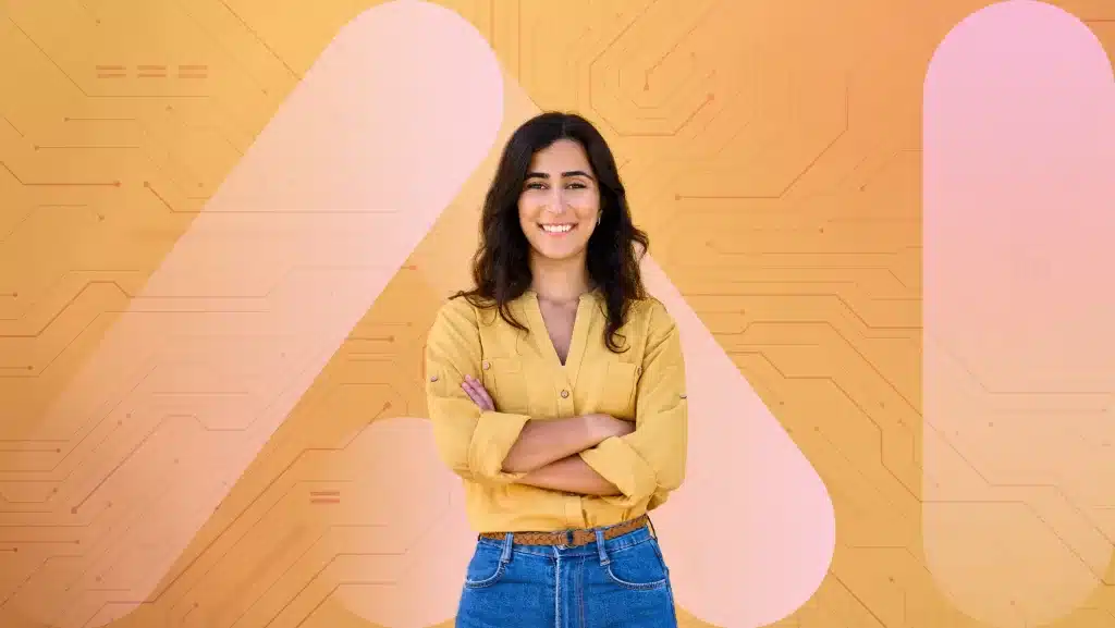 A person with long dark hair, wearing a yellow shirt and blue jeans, stands smiling, arms crossed against a background featuring AI recruitment motifs interwoven into the circuit pattern and large abstract shapes in shades of yellow and pink.