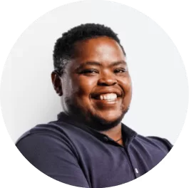 A man with short black hair and a beard smiles warmly, wearing a dark navy collared shirt against a plain white background.